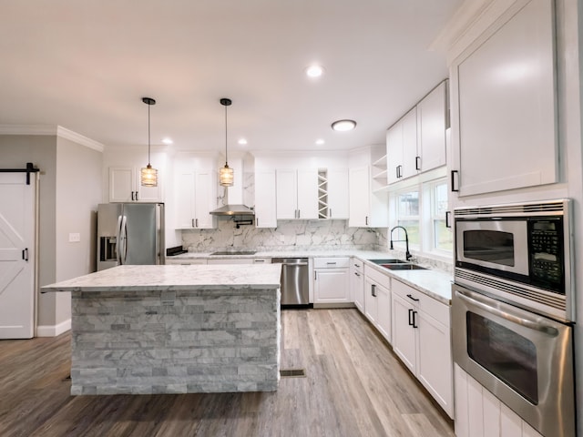 kitchen featuring a center island, a barn door, appliances with stainless steel finishes, decorative light fixtures, and white cabinetry