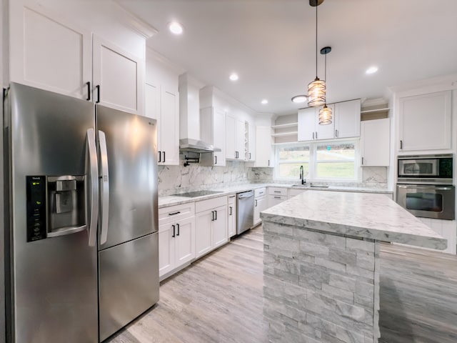 kitchen with stainless steel appliances, a sink, white cabinets, wall chimney range hood, and tasteful backsplash