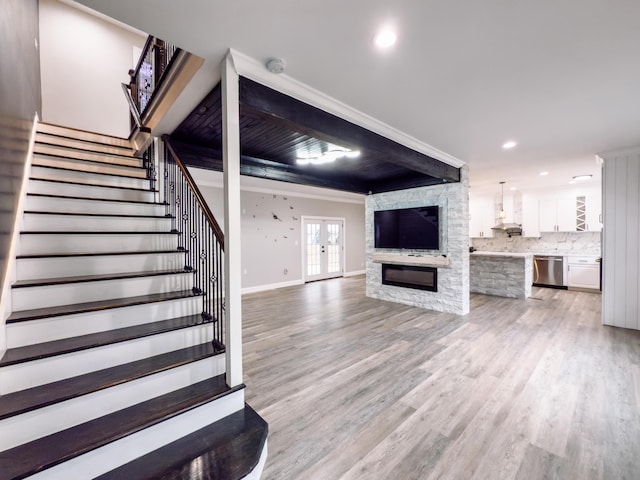 unfurnished living room with a stone fireplace, ornamental molding, light wood-type flooring, and french doors