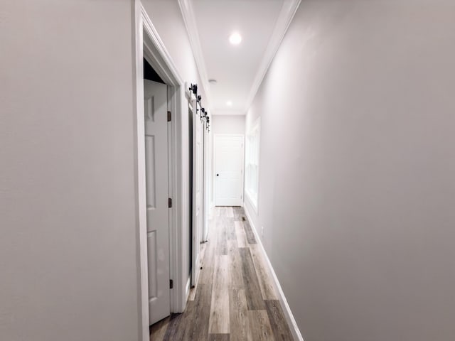 hall with recessed lighting, a barn door, ornamental molding, wood finished floors, and baseboards