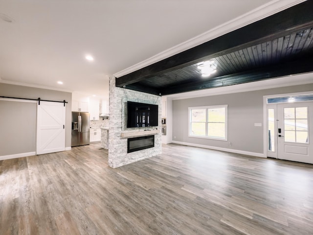 unfurnished living room with a fireplace, a barn door, light hardwood / wood-style flooring, and crown molding