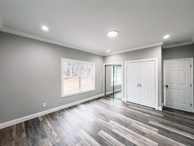 unfurnished bedroom with crown molding, baseboards, two closets, and wood finished floors