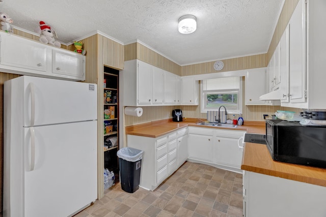 kitchen featuring white refrigerator, sink, a textured ceiling, custom range hood, and white cabinetry