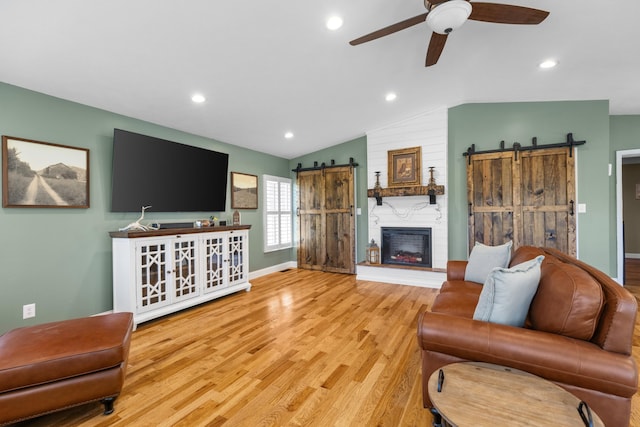 living room featuring ceiling fan, a barn door, light wood-type flooring, and vaulted ceiling