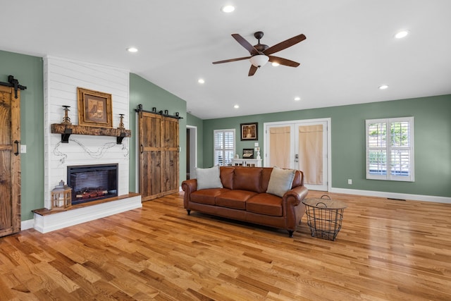 living room with light wood-type flooring, a large fireplace, ceiling fan, a barn door, and lofted ceiling