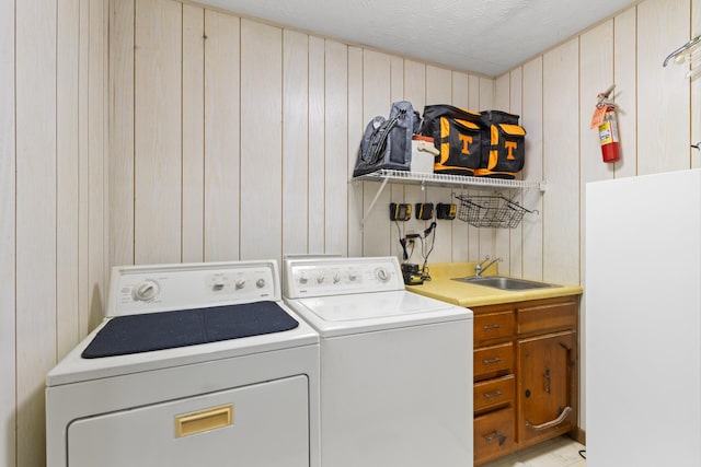 washroom featuring washer and dryer, wood walls, cabinets, and sink