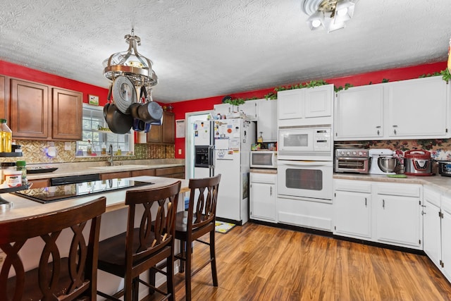 kitchen with tasteful backsplash, white appliances, sink, light hardwood / wood-style flooring, and white cabinets