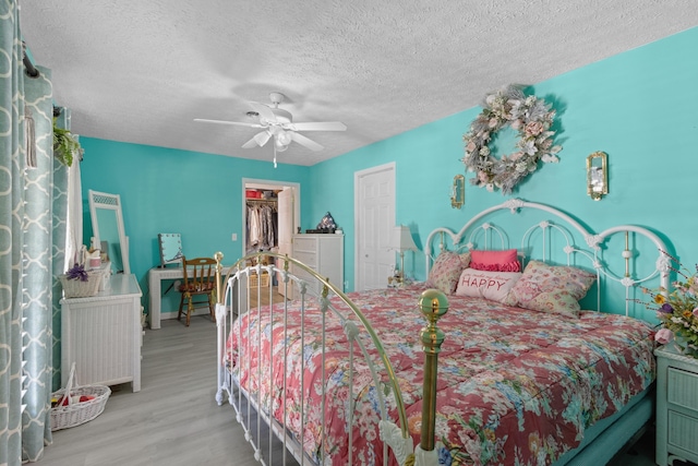 bedroom featuring a walk in closet, a textured ceiling, ceiling fan, light hardwood / wood-style flooring, and a closet