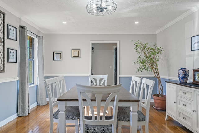 dining room featuring a textured ceiling, hardwood / wood-style floors, ornamental molding, and baseboards