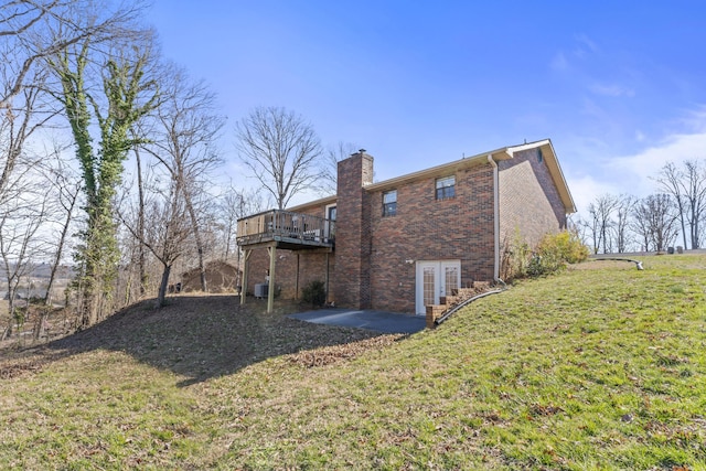 view of side of home with brick siding, a chimney, a lawn, a patio area, and a deck