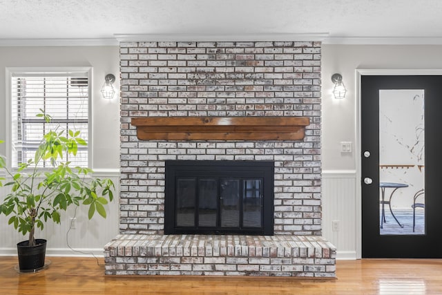 details with wainscoting, wood finished floors, a textured ceiling, crown molding, and a fireplace