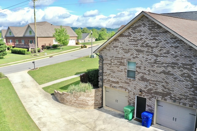 view of side of home with a yard, a garage, brick siding, and driveway