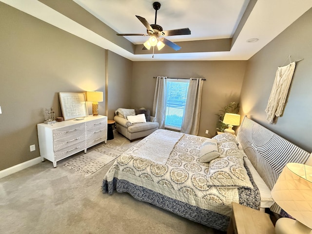 carpeted bedroom with ceiling fan, a raised ceiling, and baseboards