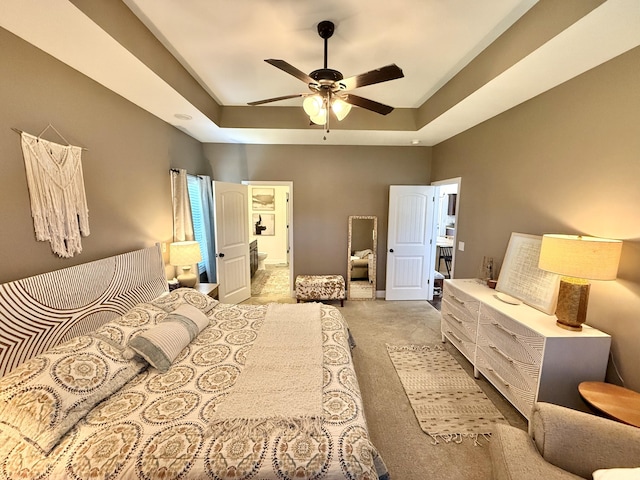 bedroom featuring ensuite bathroom, light carpet, a tray ceiling, and ceiling fan