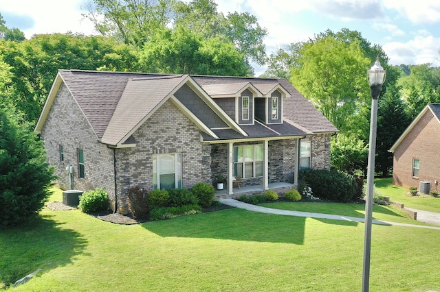 craftsman-style home featuring central AC unit, a shingled roof, brick siding, and a front yard