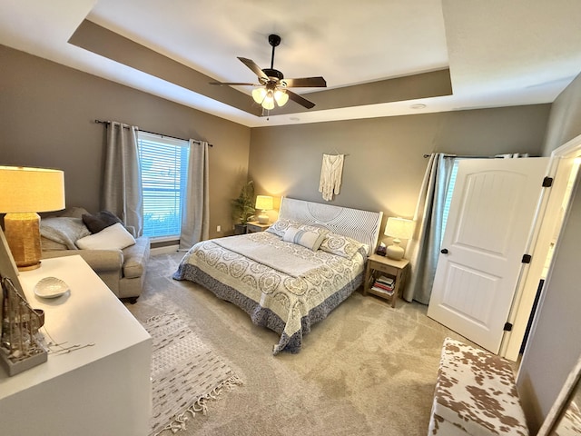 bedroom featuring a ceiling fan, light carpet, and a tray ceiling