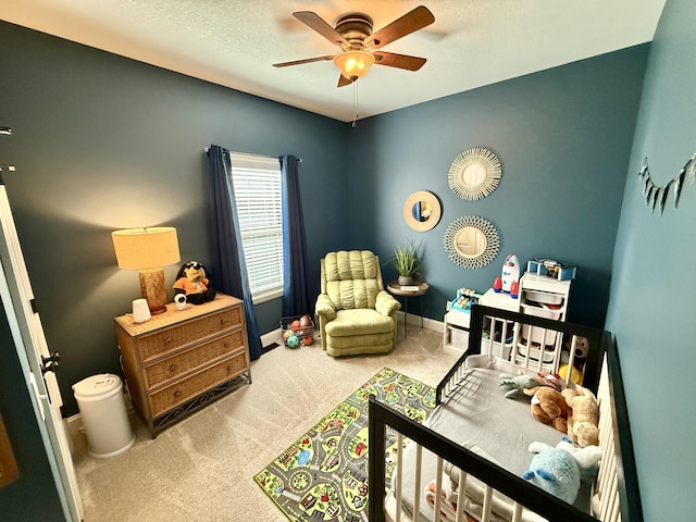 carpeted bedroom featuring a nursery area, baseboards, and ceiling fan