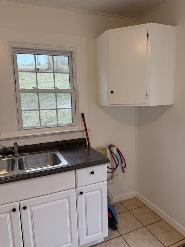 kitchen featuring light tile patterned floors, a sink, white cabinetry, baseboards, and dark countertops