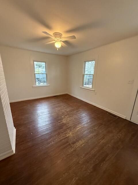 empty room featuring dark wood-style floors, visible vents, ceiling fan, and baseboards