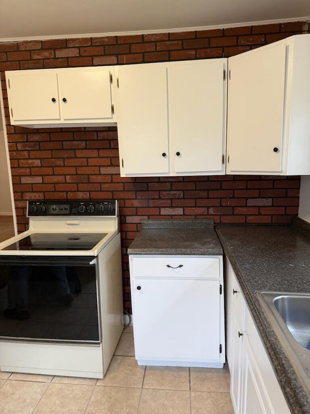 kitchen with dark countertops, electric range, white cabinetry, a sink, and light tile patterned flooring