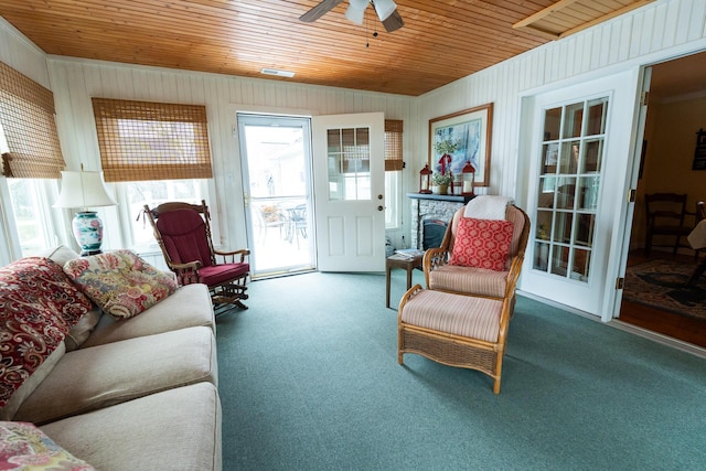 living room featuring carpet flooring, ceiling fan, wood ceiling, and a stone fireplace