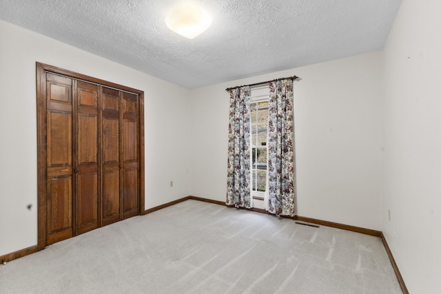 unfurnished bedroom featuring light carpet, a textured ceiling, and a closet