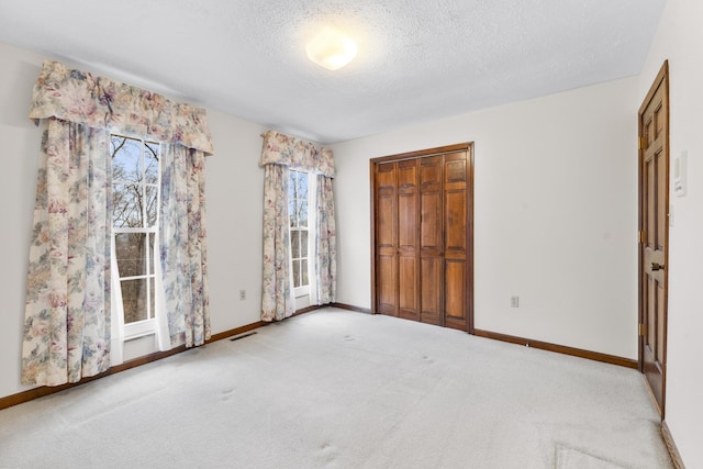 unfurnished bedroom featuring light colored carpet, a textured ceiling, and a closet