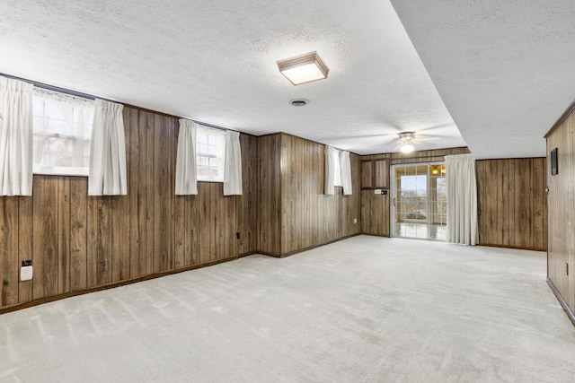 basement with a textured ceiling, wooden walls, light colored carpet, and a healthy amount of sunlight