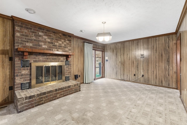 unfurnished living room with wood walls, light carpet, a brick fireplace, ornamental molding, and a textured ceiling