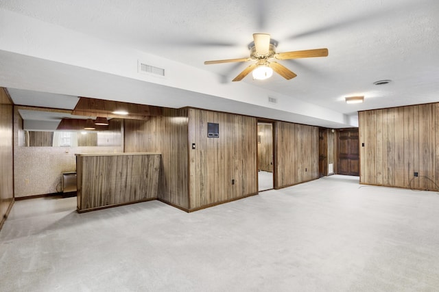 basement with ceiling fan, wood walls, light colored carpet, and a textured ceiling