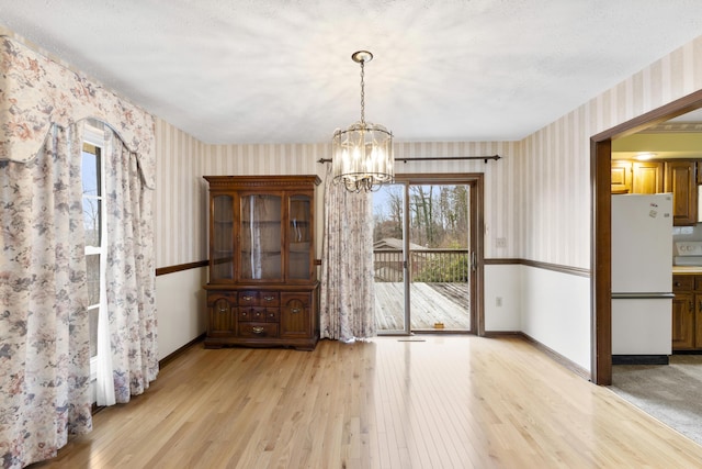 unfurnished dining area featuring a notable chandelier, light hardwood / wood-style floors, and a textured ceiling