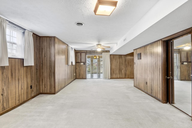 spare room with a textured ceiling, ceiling fan, light carpet, and wooden walls