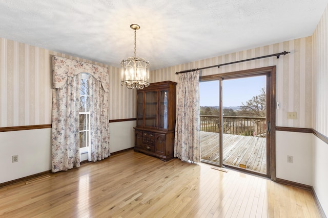 unfurnished dining area featuring light hardwood / wood-style floors, a textured ceiling, and a chandelier