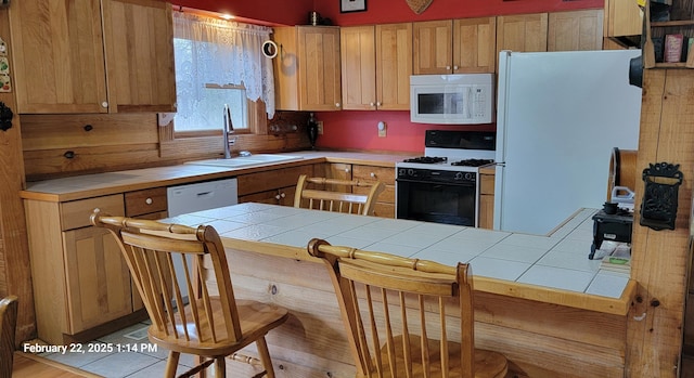 kitchen with tile countertops, a peninsula, white appliances, a sink, and a kitchen bar