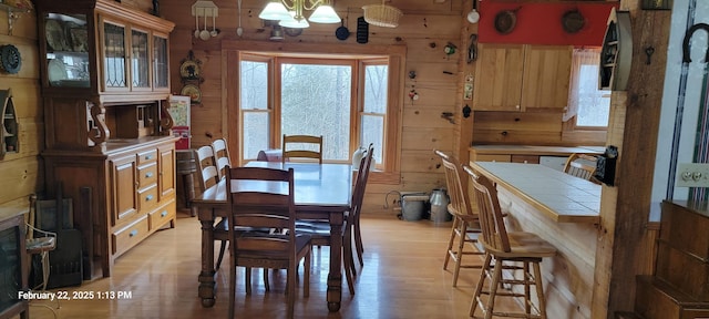 dining room with a healthy amount of sunlight, wood walls, light wood-style flooring, and a notable chandelier