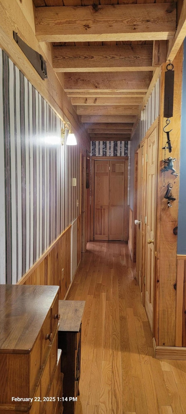 hall featuring light wood-style floors, beamed ceiling, and wood walls