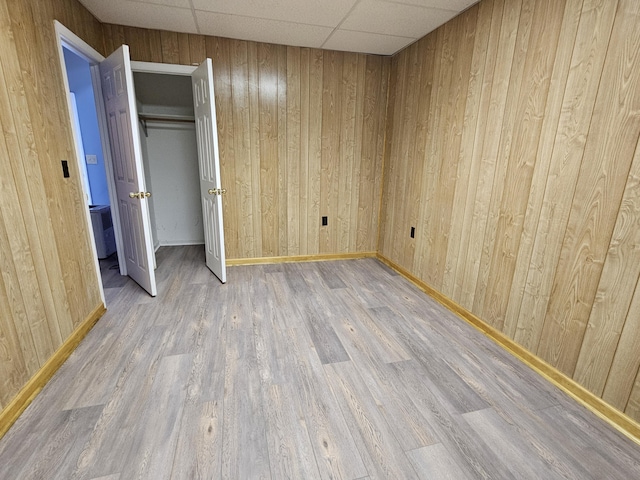 unfurnished bedroom featuring a paneled ceiling, hardwood / wood-style flooring, and wood walls