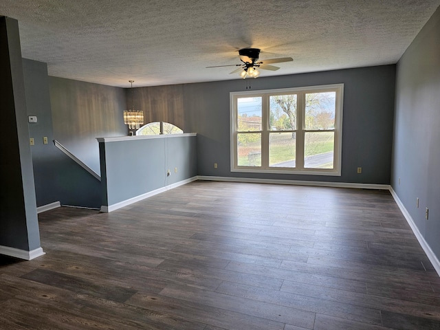 empty room with ceiling fan with notable chandelier, a textured ceiling, and dark hardwood / wood-style flooring