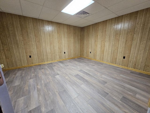 spare room with a paneled ceiling, wooden walls, and hardwood / wood-style flooring