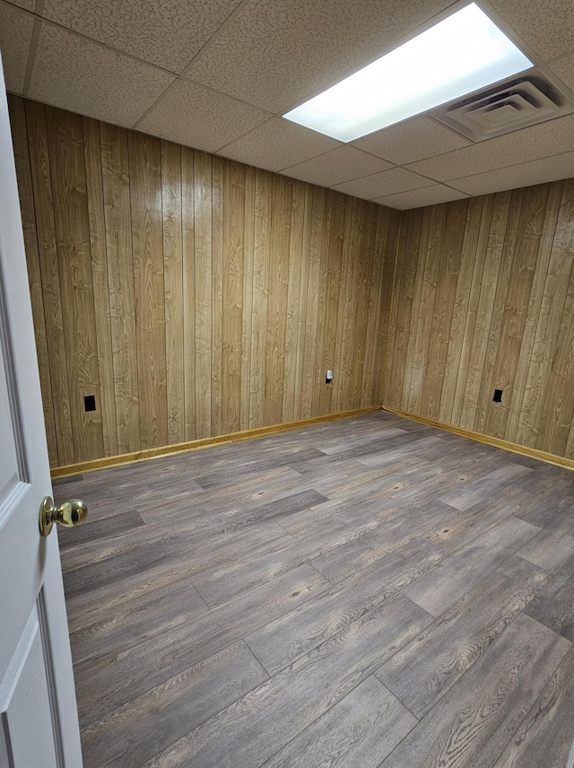 unfurnished room with hardwood / wood-style floors, a paneled ceiling, and wooden walls