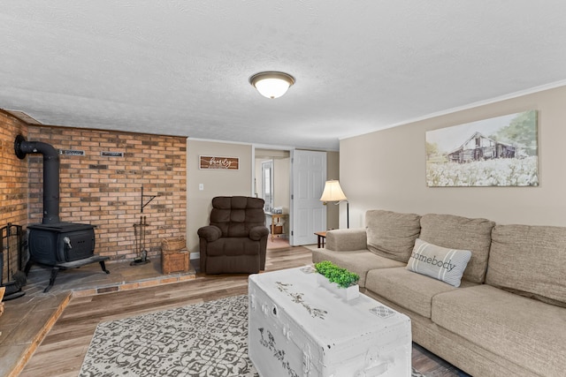 living room with a textured ceiling, ornamental molding, wood finished floors, and a wood stove