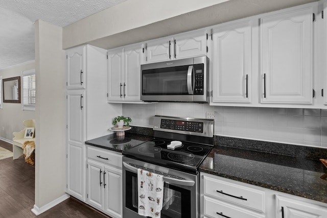 kitchen featuring stainless steel appliances, dark wood-type flooring, white cabinets, tasteful backsplash, and dark stone countertops