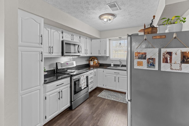 kitchen with a sink, white cabinetry, appliances with stainless steel finishes, dark wood-style floors, and dark countertops