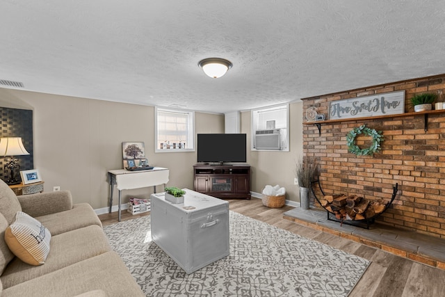 living room featuring baseboards, visible vents, light wood-style flooring, cooling unit, and a textured ceiling