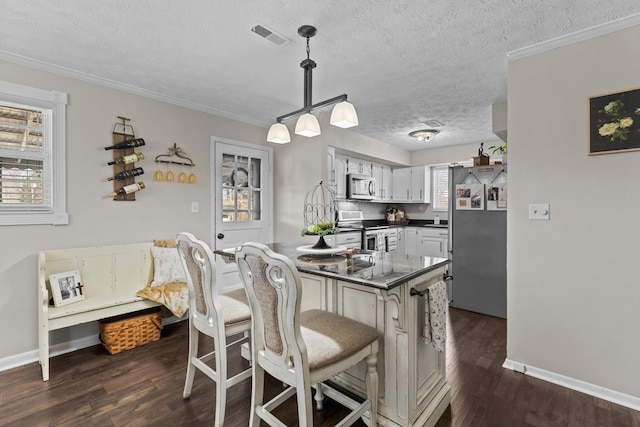 kitchen with dark wood-style flooring, white cabinetry, a kitchen breakfast bar, appliances with stainless steel finishes, and dark countertops