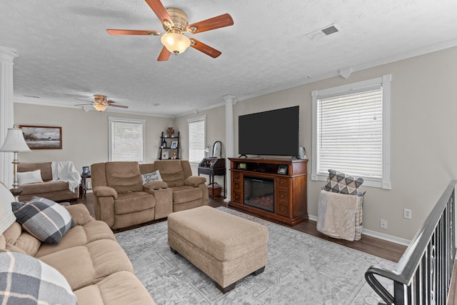 living area with ornamental molding, a glass covered fireplace, light wood finished floors, and ornate columns