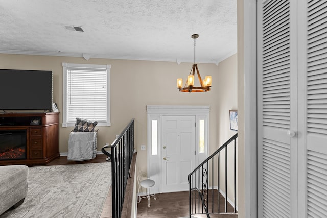 foyer featuring dark wood-style flooring, crown molding, visible vents, an inviting chandelier, and a textured ceiling