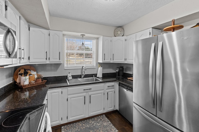 kitchen with dark wood finished floors, stainless steel appliances, dark countertops, white cabinetry, and a sink