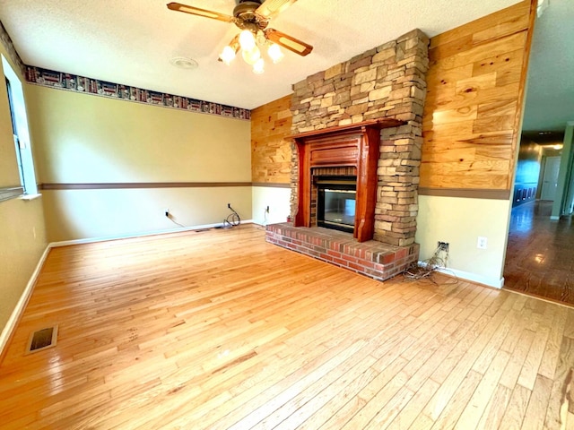 unfurnished living room with a large fireplace, hardwood / wood-style floors, a ceiling fan, baseboards, and visible vents
