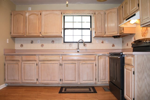 kitchen with light brown cabinetry, a sink, light countertops, under cabinet range hood, and black range with electric stovetop